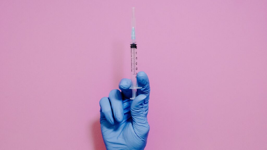 Gloved hand holding syringe with a pink background